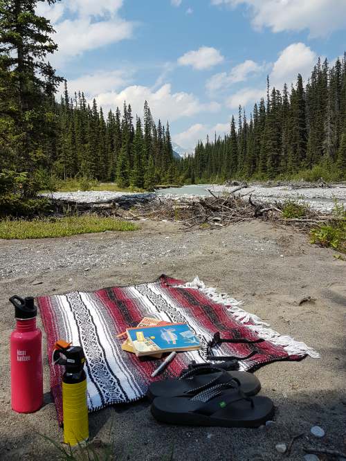 A blanket and books sit on a riverbank