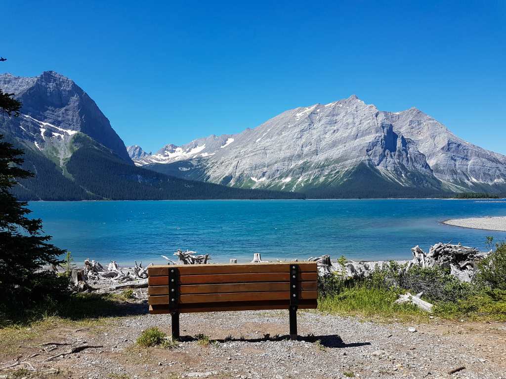 A bench sits in front of a lake with mountains in the background