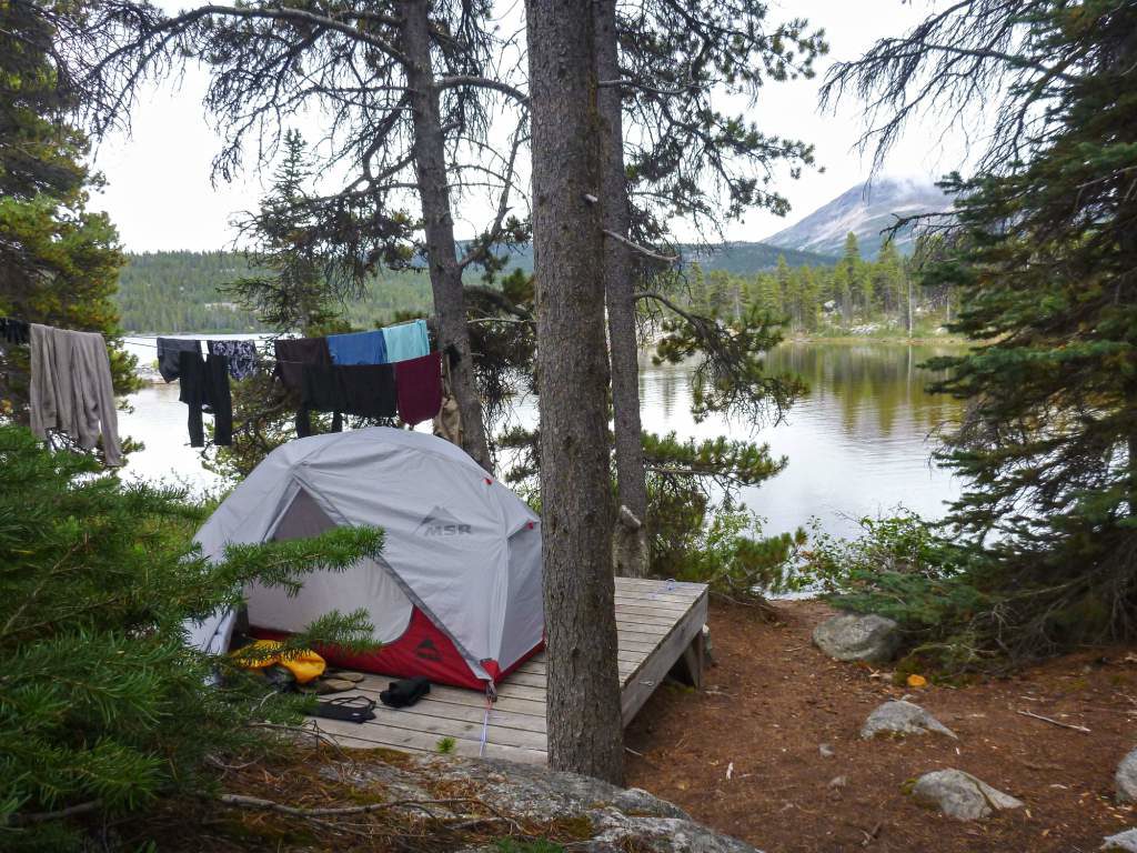 A tent and clothesline sit on the edge of a lake