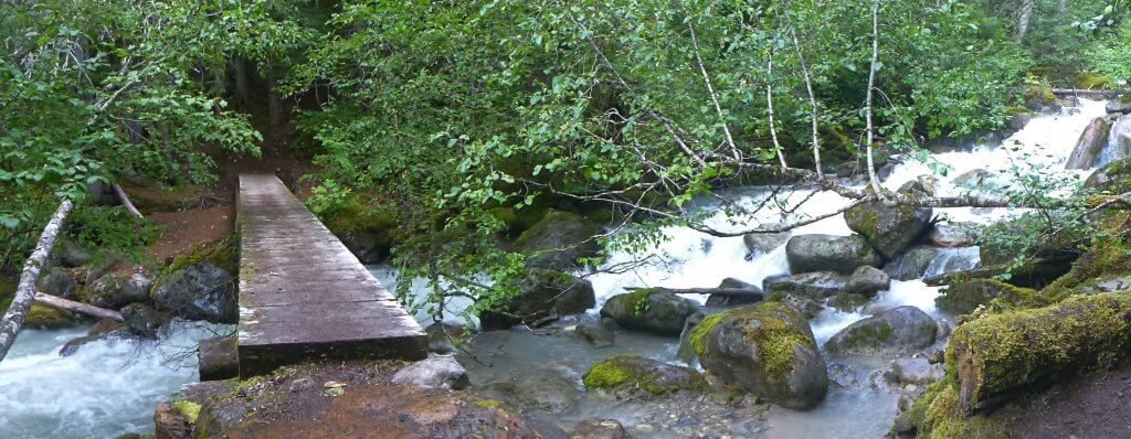 A wooden bridge spans the river on the Chilkoot Trail