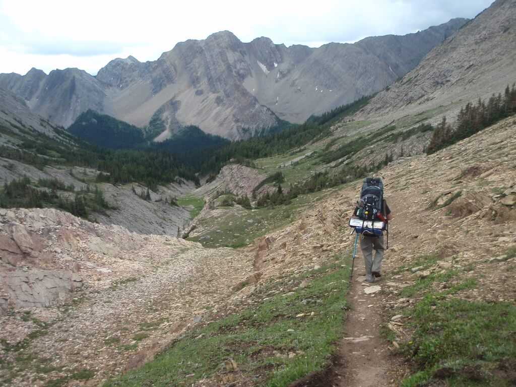 A backpacker walks along a trail surrounded by rocky mountains 