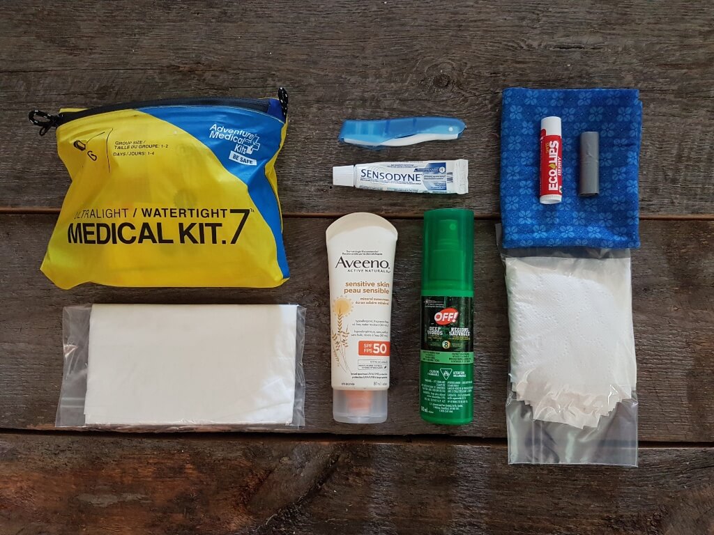A first aid kit and toiletries are laid out ready to be packed for a backpacking trip.
