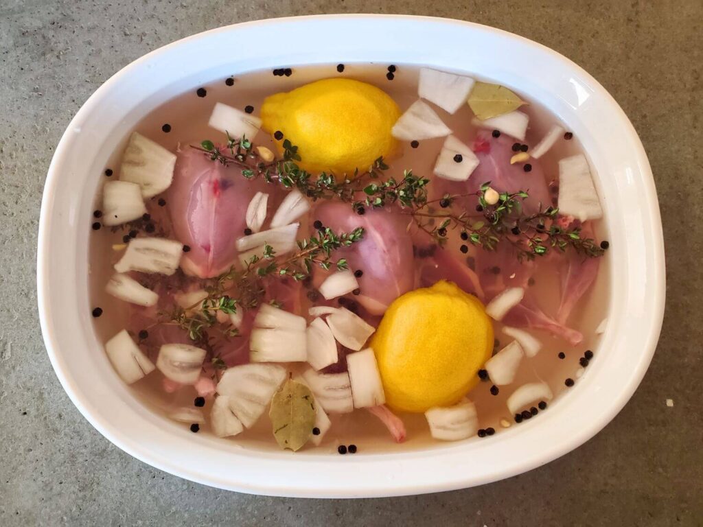 Quail meat brines in a dish with onions, spices, lemons.