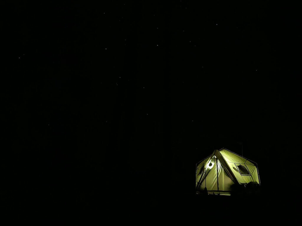 A tent lit up at night with stars in the background